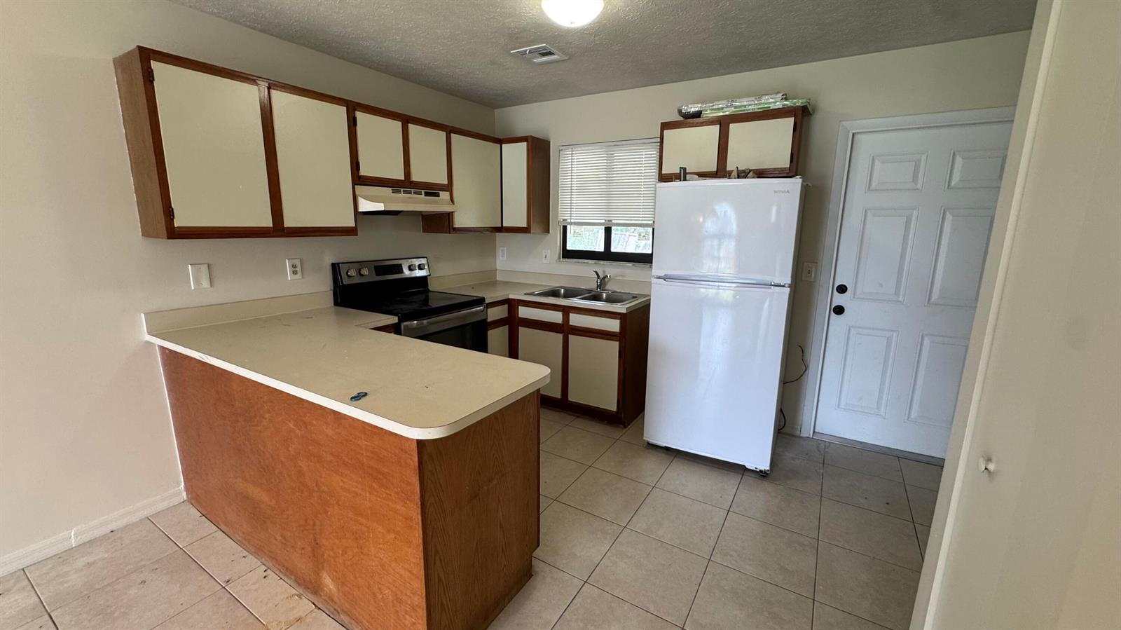 A kitchen features white and wood-toned cabinets, a white refrigerator, and a tiled floor — 5045 SE Primrose Way, Stuart FL 34997, STUART, FL