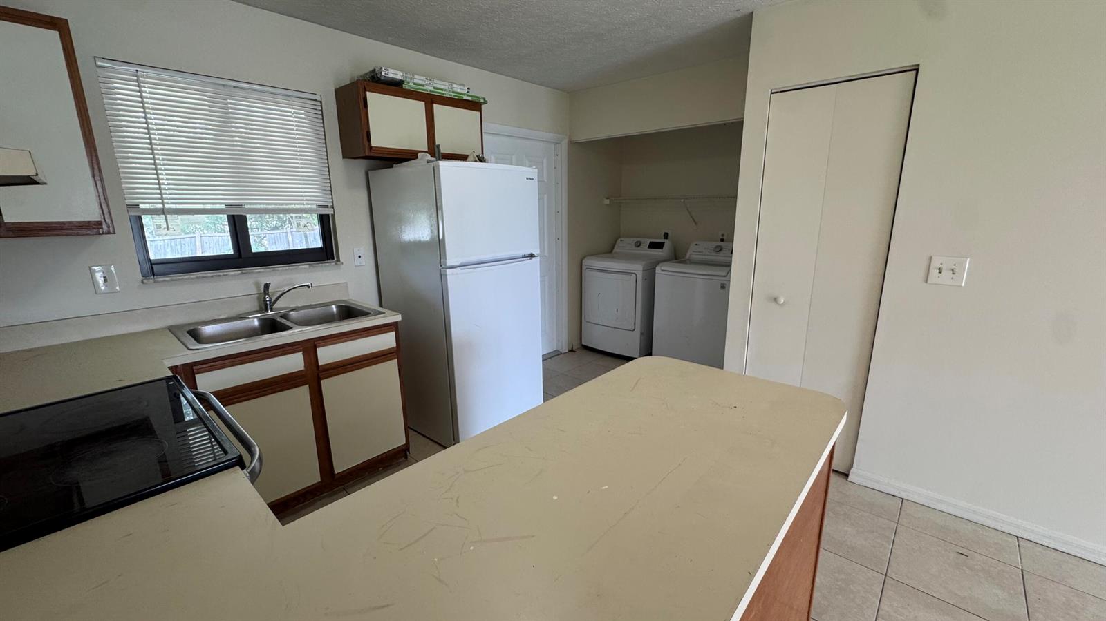 A kitchen features a sink, refrigerator, laundry appliances, and a peninsula counter with beige surfaces — 5045 SE Primrose Way, Stuart FL 34997, STUART, FL