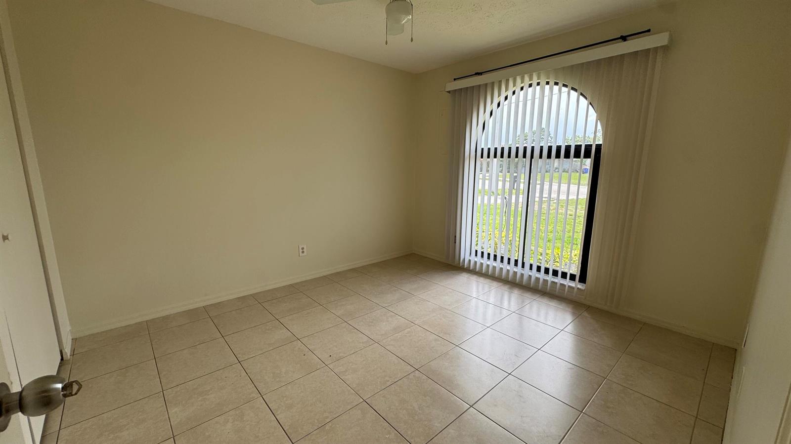 An empty room with beige tile flooring and a large arched window with vertical blinds — 5045 SE Primrose Way, Stuart FL 34997, STUART, FL