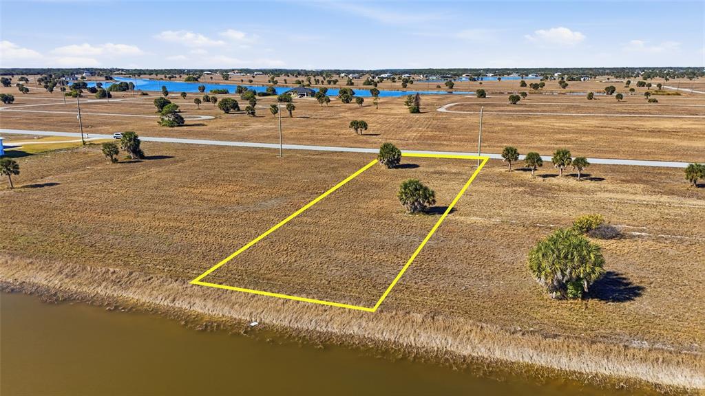 An aerial view shows a vacant, rectangular lot outlined in yellow bordering a small pond — 32 YELLOWHAMMER DRIVE, PLACIDA, FL