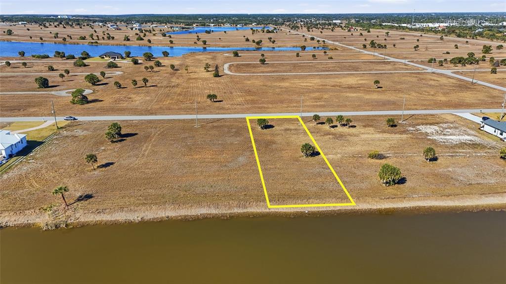 An aerial view shows a rectangular vacant lot outlined in yellow bordering a lake — 32 YELLOWHAMMER DRIVE, PLACIDA, FL