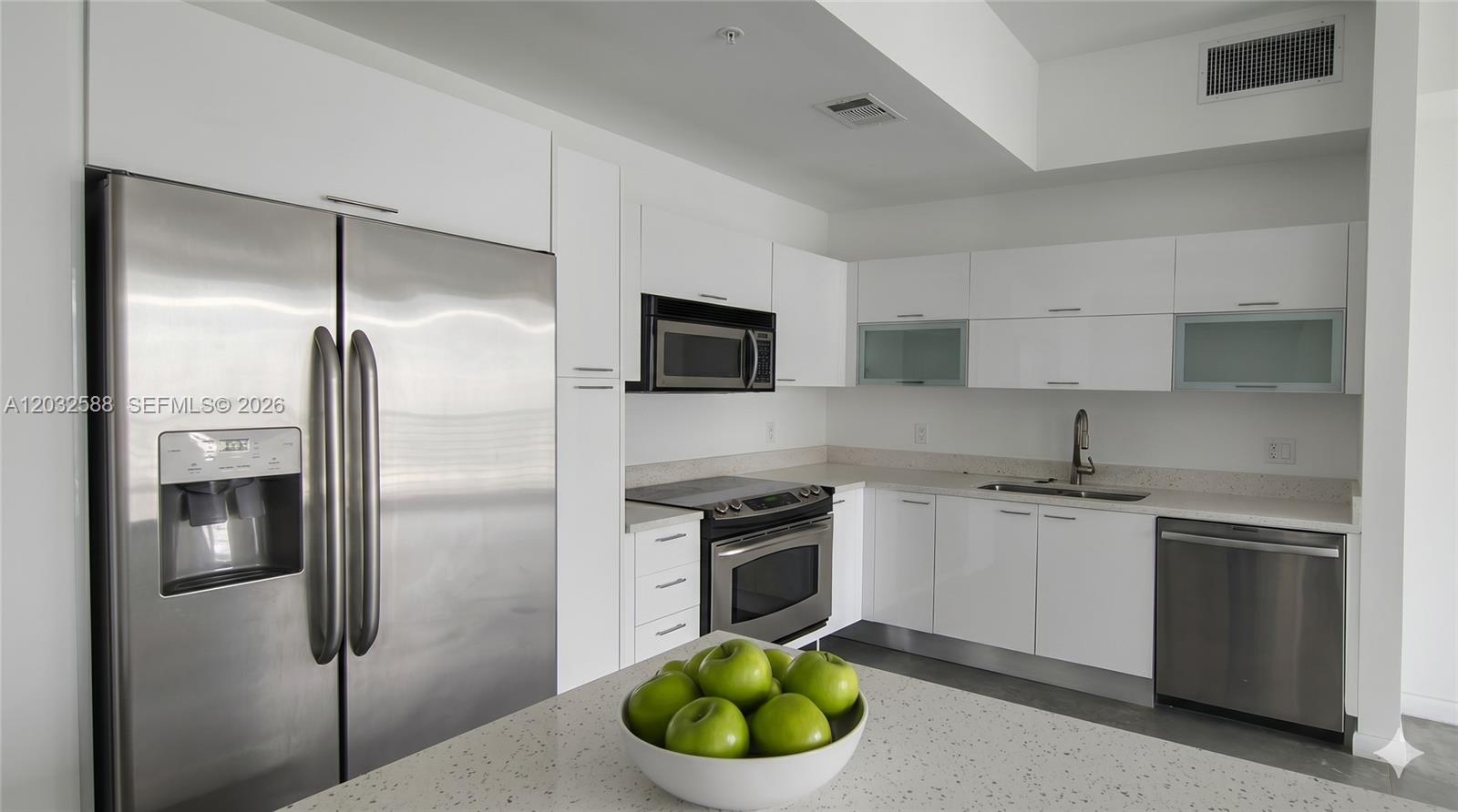 A modern kitchen features white cabinets, stainless steel appliances, and a speckled countertop island — 133 NE 2nd Ave # 1906, Miami FL 33132, MIAMI, FL
