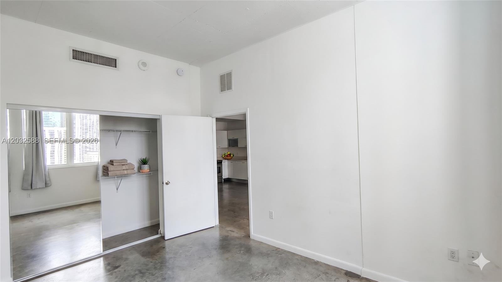 An interior room features concrete floors, a mirrored closet, and an open doorway to a kitchen — 133 NE 2nd Ave # 1906, Miami FL 33132, MIAMI, FL