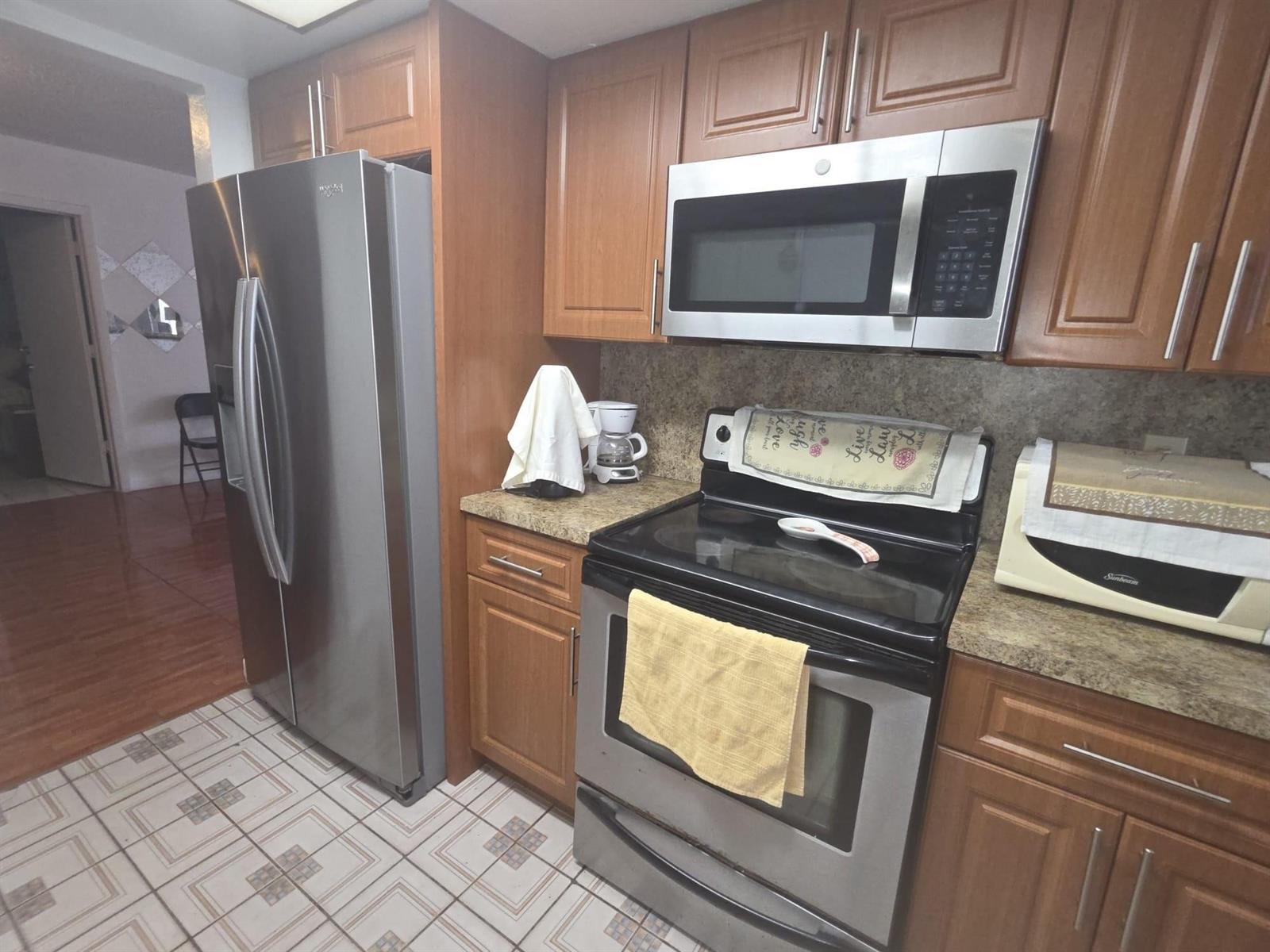 A kitchen features stainless steel appliances, wood cabinets, and a tiled floor — 5261 NW 14th Place, Lauderhill FL 33313, LAUDERHILL, FL