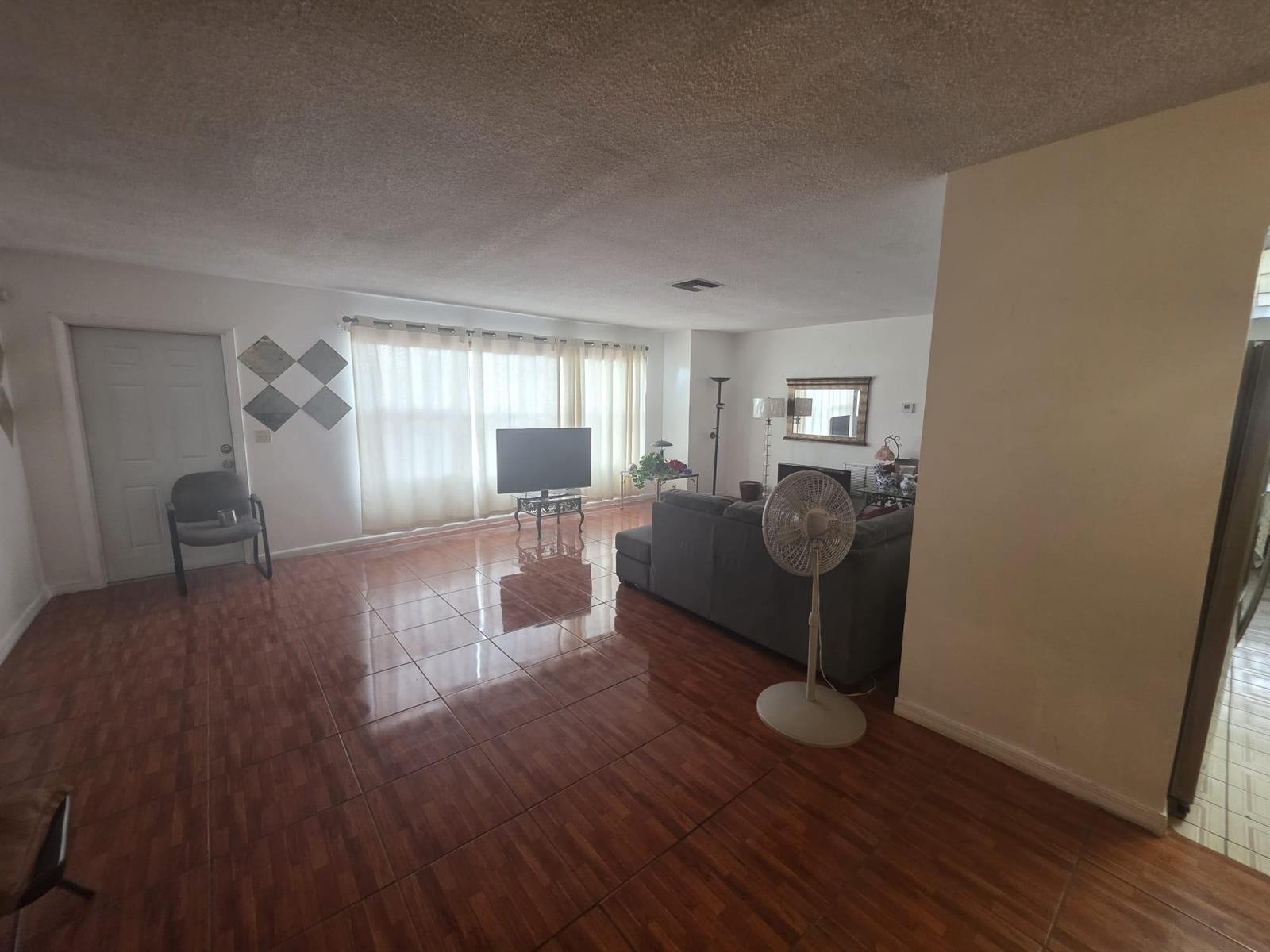 A living room with glossy brown tile flooring, a grey sectional sofa, and large windows — 5261 NW 14th Place, Lauderhill FL 33313, LAUDERHILL, FL