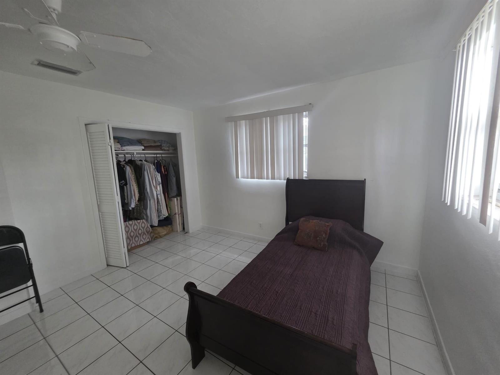 A bedroom with white tile floors, a dark wood bed frame, and a walk-in closet — 5261 NW 14th Place, Lauderhill FL 33313, LAUDERHILL, FL