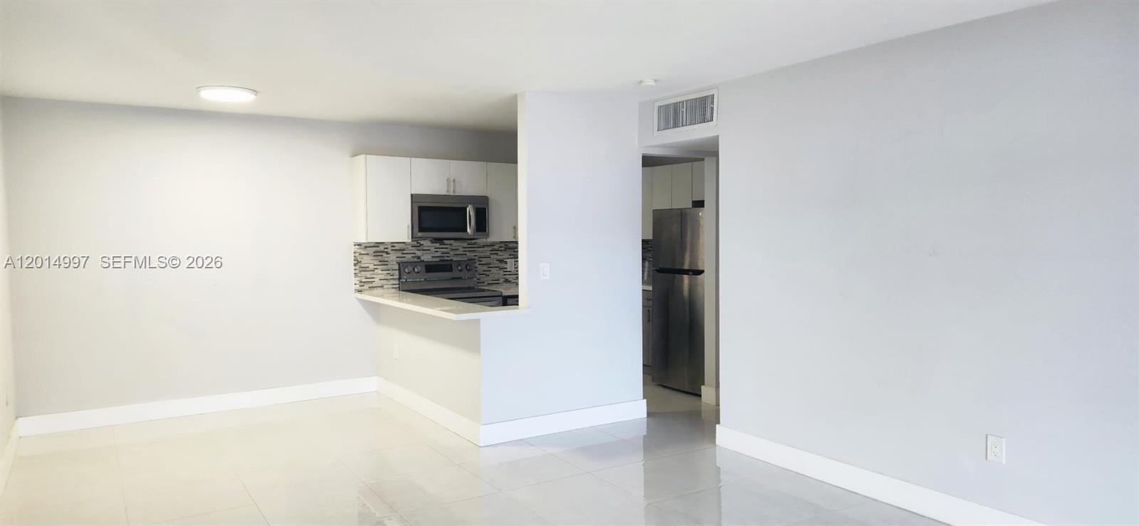 A kitchen with stainless steel appliances and white cabinets opens to a tiled living area — 7823 Miller Dr # C105, Miami FL 33155, MIAMI, FL