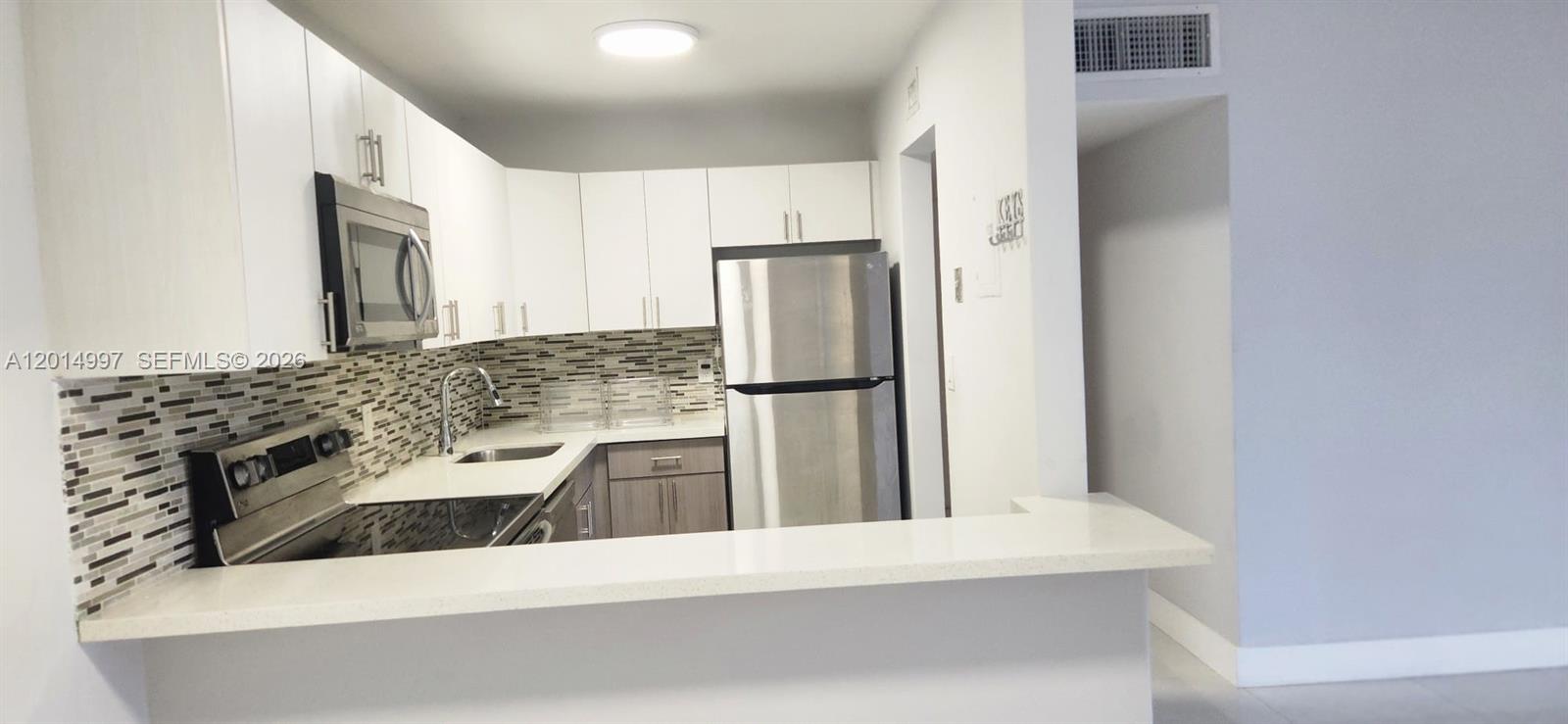 A kitchen features white upper cabinets, gray lower cabinets, stainless steel appliances, and tiled backsplash — 7823 Miller Dr # C105, Miami FL 33155, MIAMI, FL