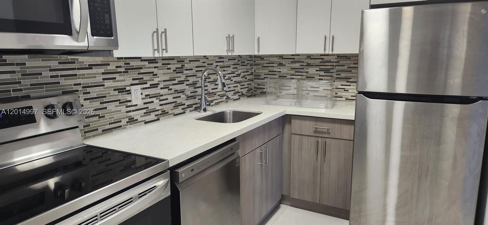 A kitchen features white upper cabinets, wood-tone lower cabinets, stainless steel appliances, and tiled backsplash — 7823 Miller Dr # C105, Miami FL 33155, MIAMI, FL