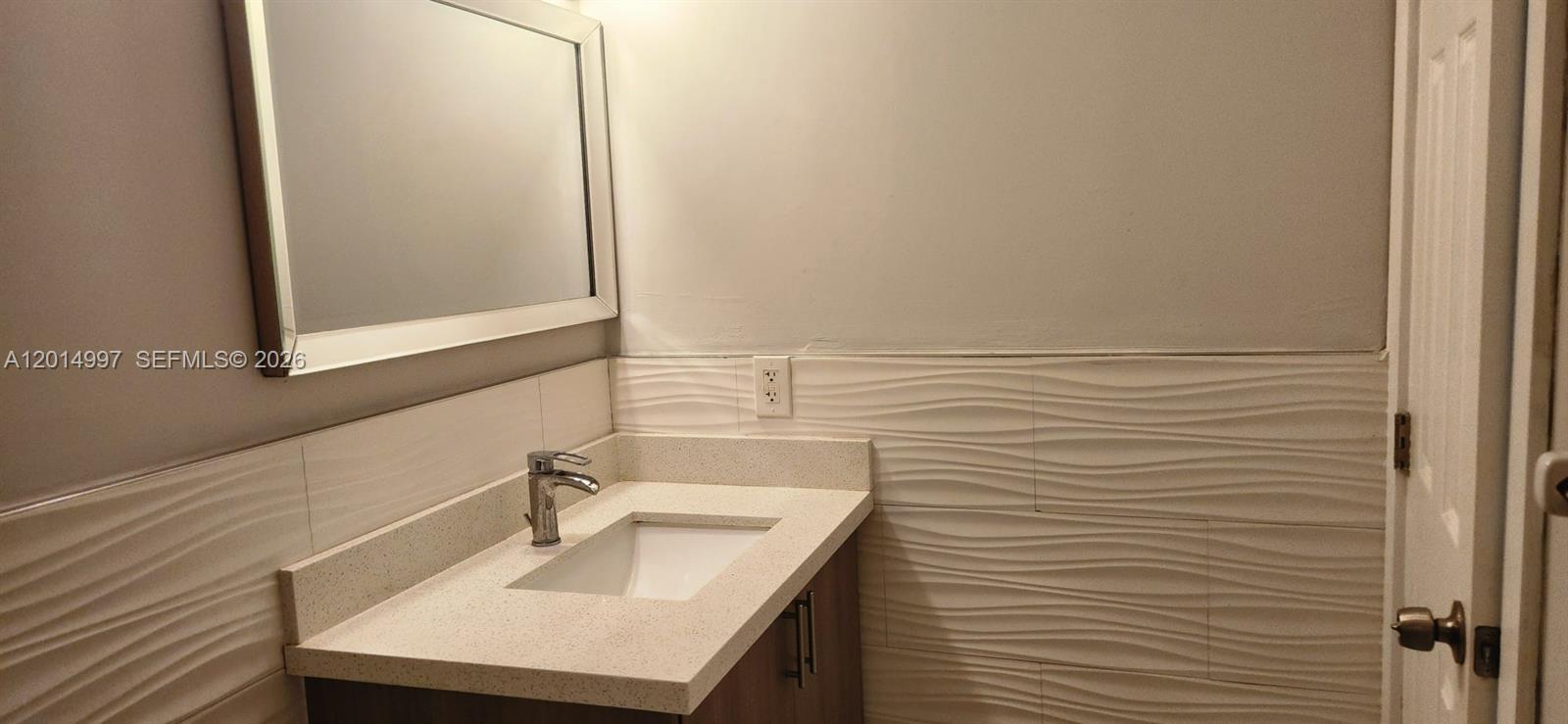 A bathroom features a vanity with a white countertop, a mirror, and textured wall tiles — 7823 Miller Dr # C105, Miami FL 33155, MIAMI, FL