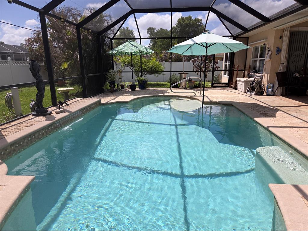 A swimming pool with a screened-in enclosure, patio, and two umbrellas in a backyard — 32 ORLANDO BOULEVARD, PORT CHARLOTTE, FL