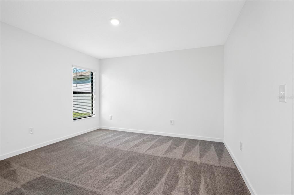 An empty bedroom features white walls, gray carpet, and a single window with blinds — 537 BLACKTHORN DRIVE, LAKELAND, FL