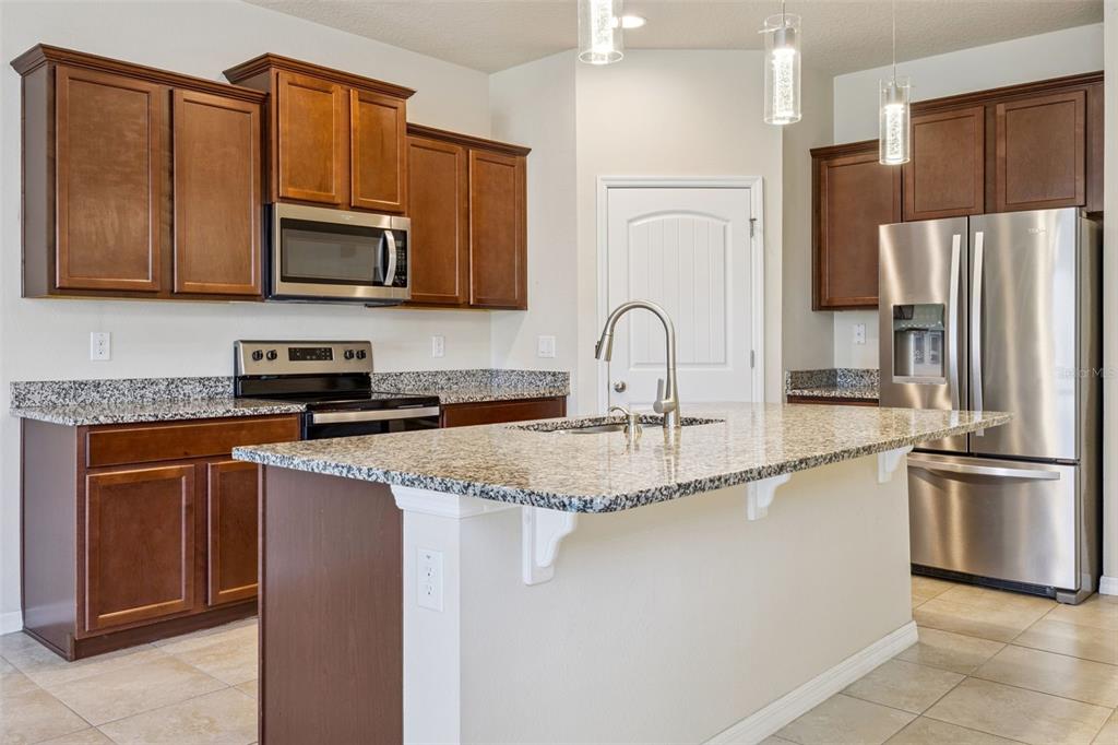 A kitchen featuring dark wood cabinets, granite countertops, stainless steel appliances, and a central island — 10294 MERRYMEETING BAY DRIVE, WINTER GARDEN, FL