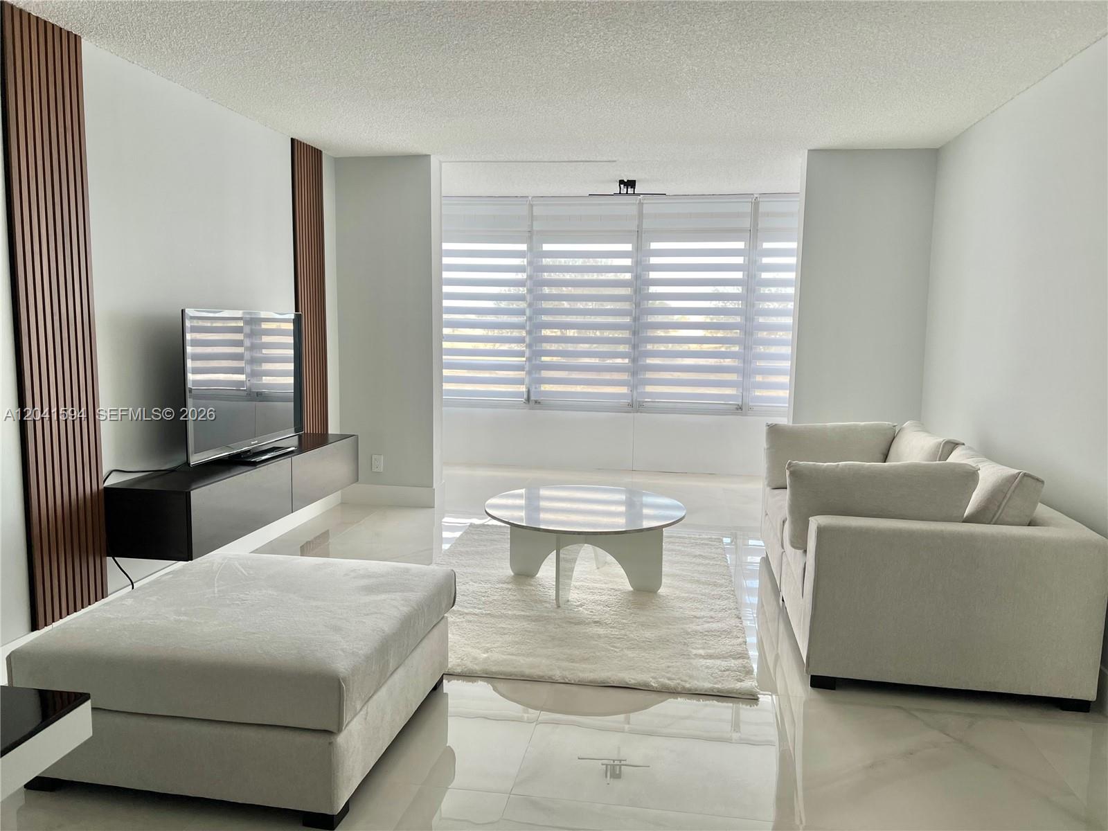 A living room features a white sofa, a round coffee table, and a wall-mounted television — 2551 Aragon Blvd # 310, Sunrise FL 33322, SUNRISE, FL