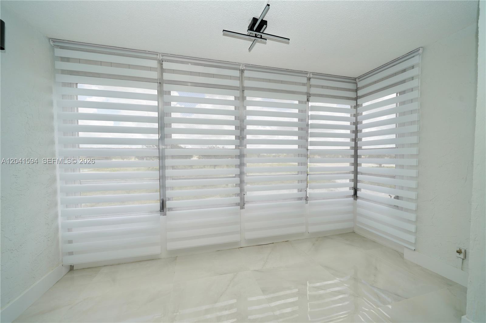 A bright room features white marble floors, large windows with zebra blinds, and a ceiling light — 2551 Aragon Blvd # 310, Sunrise FL 33322, SUNRISE, FL