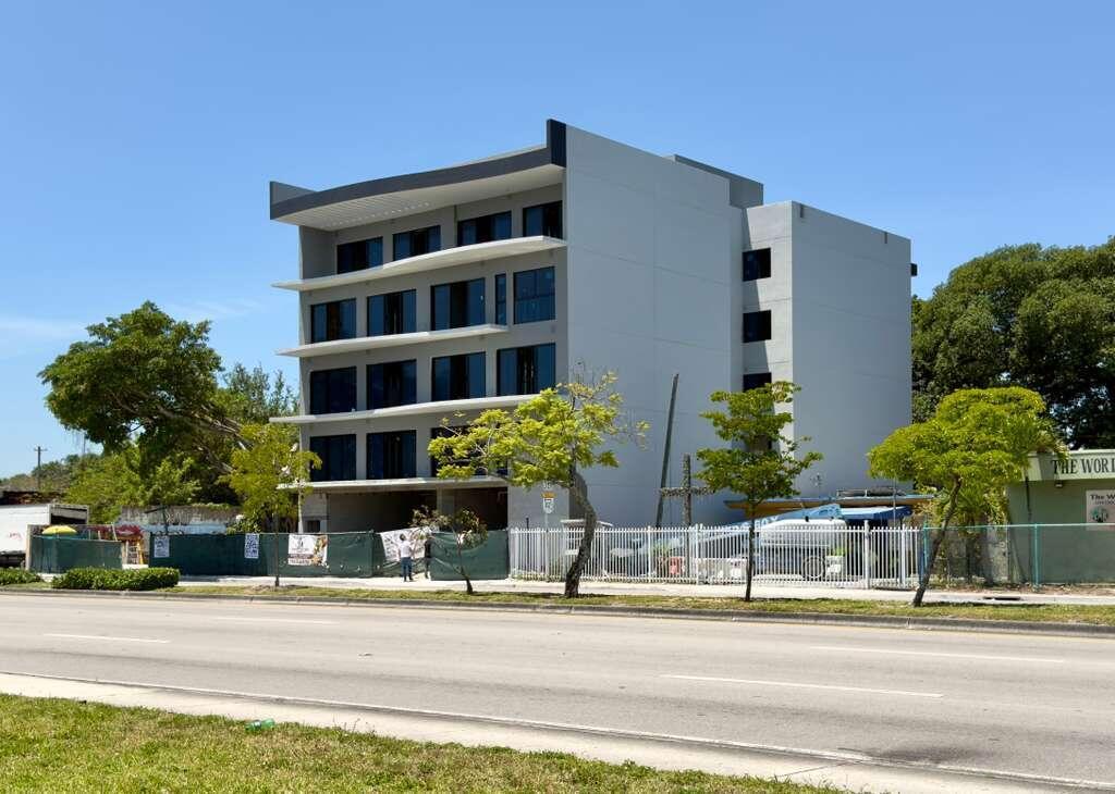 A modern, multi-story gray building under construction stands behind a white fence along a road — 4110 NW 22nd Avenue # 1, Miami FL 33142, MIAMI, FL