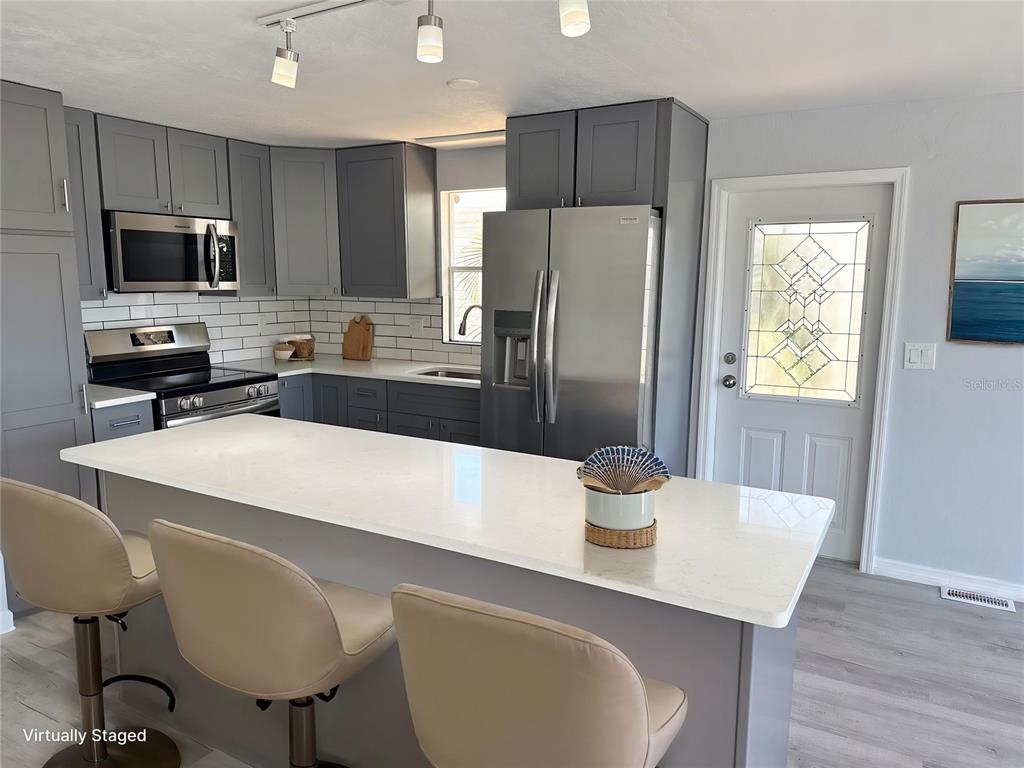 A kitchen features gray cabinets, stainless steel appliances, a white island, and a glass-paneled door — 460 MOUNT OAK AVENUE NE UNIT 745, ST PETERSBURG, FL