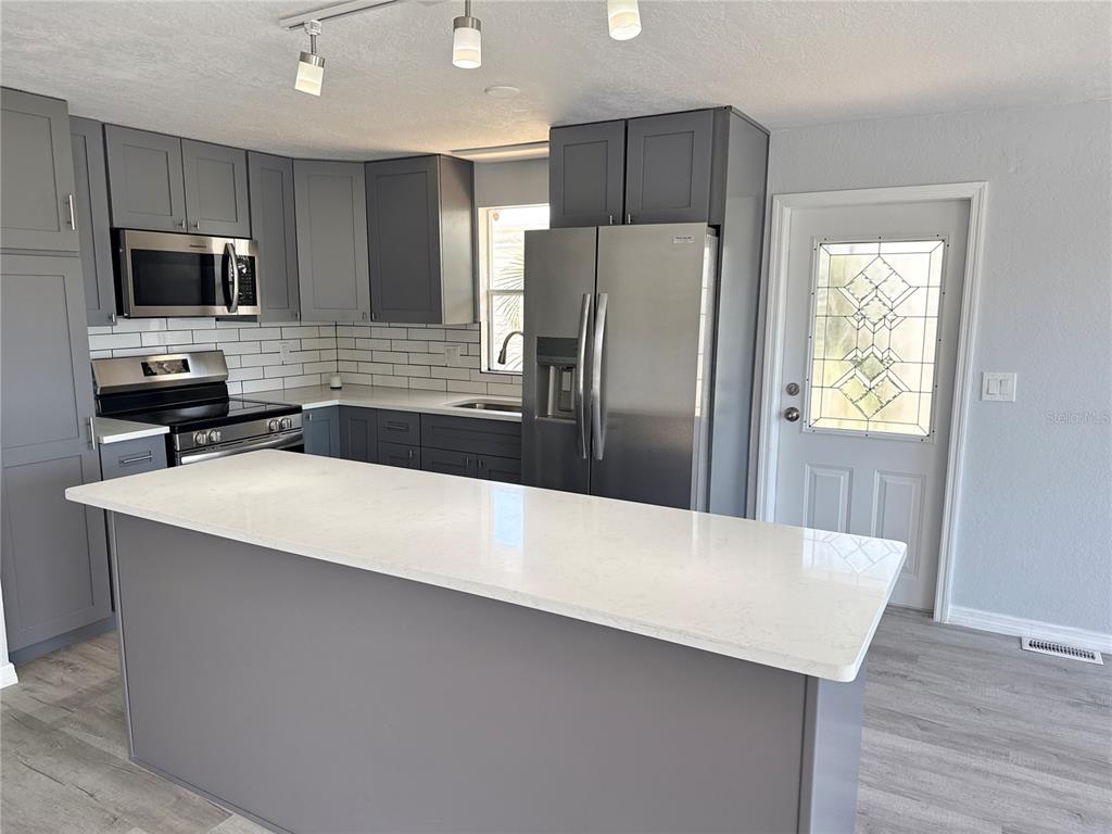 A kitchen features gray cabinets, stainless steel appliances, a white island, and a glass-paneled door — 460 MOUNT OAK AVENUE NE UNIT 745, ST PETERSBURG, FL