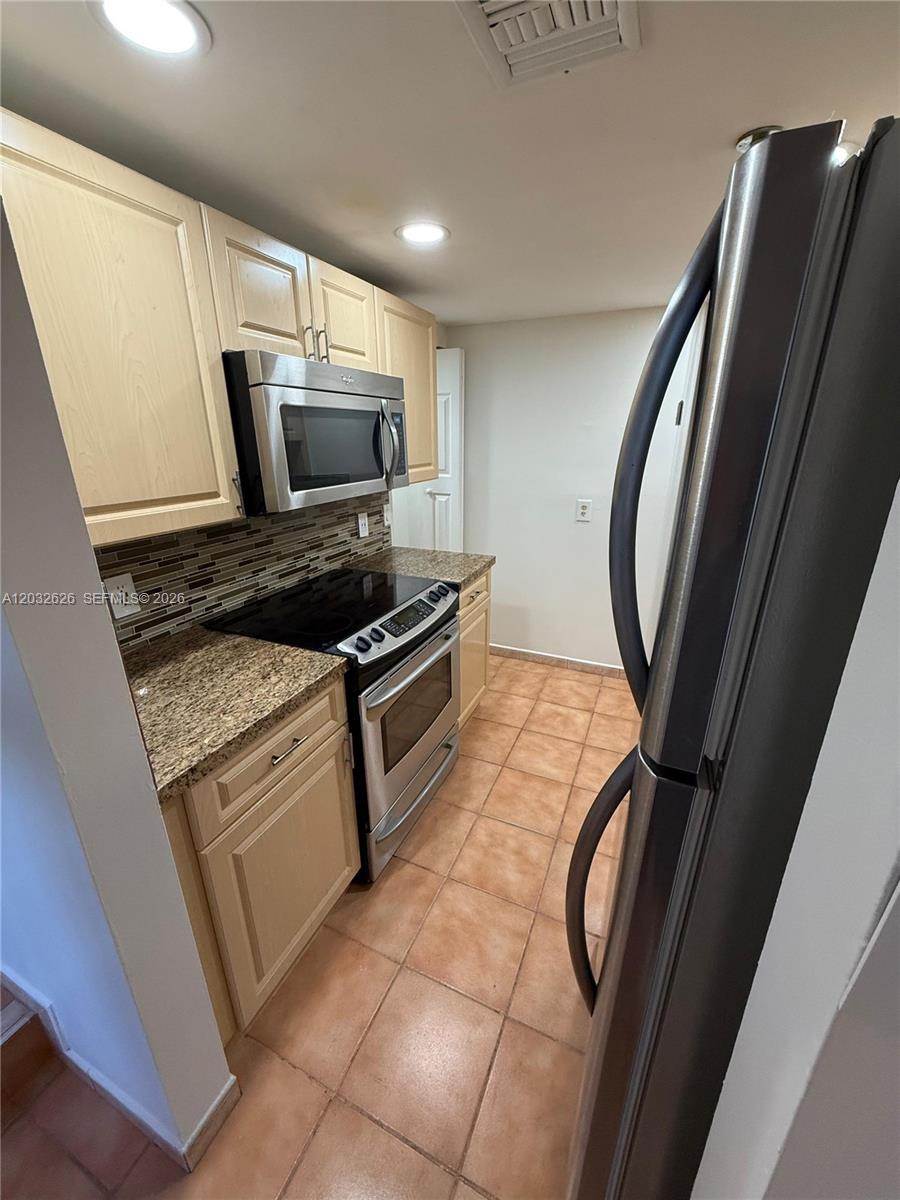 A galley kitchen features light wood cabinets, granite countertops, and stainless steel appliances — 10641 SW 108 AVE # 3I, Miami FL 33176, MIAMI, FL