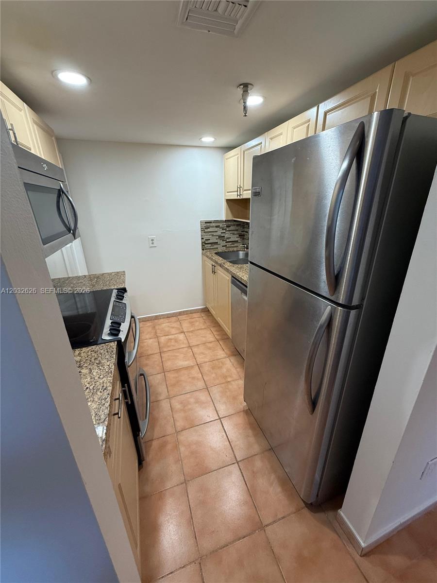 A narrow galley kitchen features stainless steel appliances, light wood cabinets, and granite countertops — 10641 SW 108 AVE # 3I, Miami FL 33176, MIAMI, FL