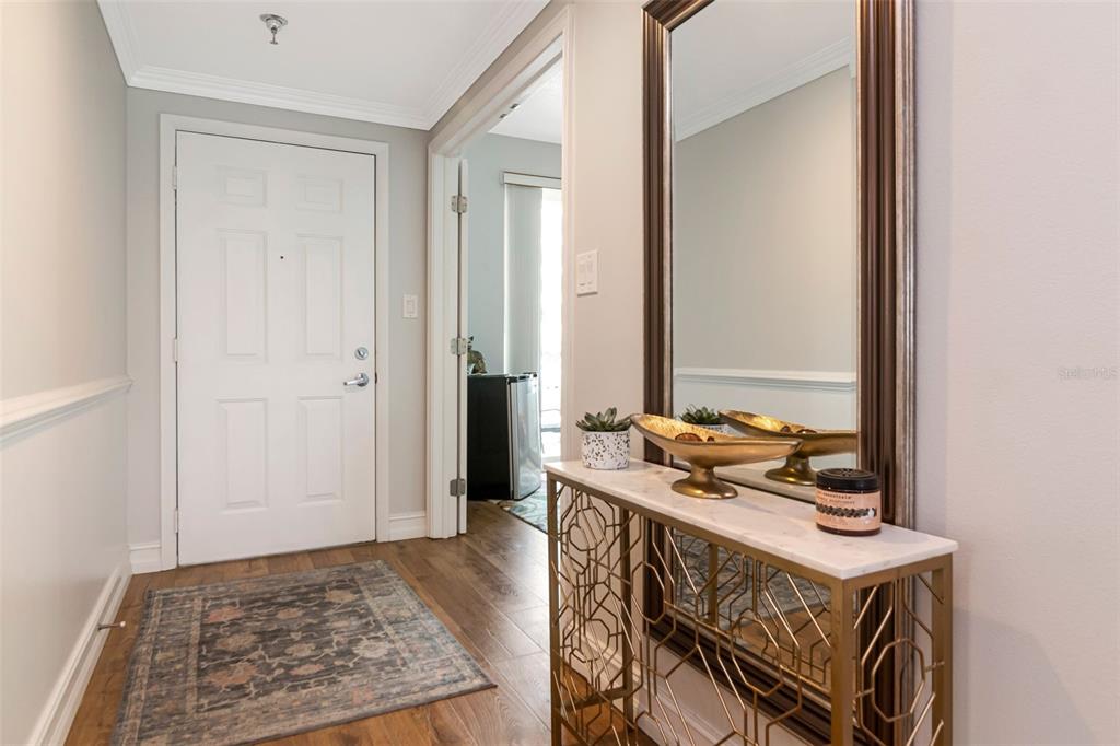 An entryway features a white door, wood flooring, a patterned rug, and a gold console table — 7979 SAILBOAT KEY BOULEVARD S UNIT 101, SOUTH PASADENA, FL