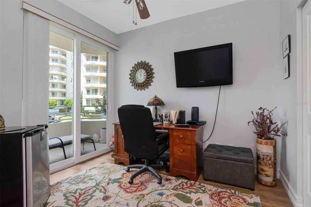 A home office features a wooden desk, a black office chair, and a balcony view — 7979 SAILBOAT KEY BOULEVARD S UNIT 101, SOUTH PASADENA, FL