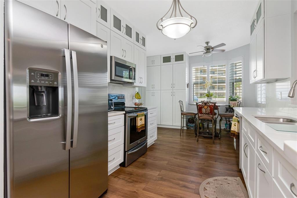 A kitchen with white cabinets, stainless steel appliances, and wood-look flooring near a dining area — 7979 SAILBOAT KEY BOULEVARD S UNIT 101, SOUTH PASADENA, FL