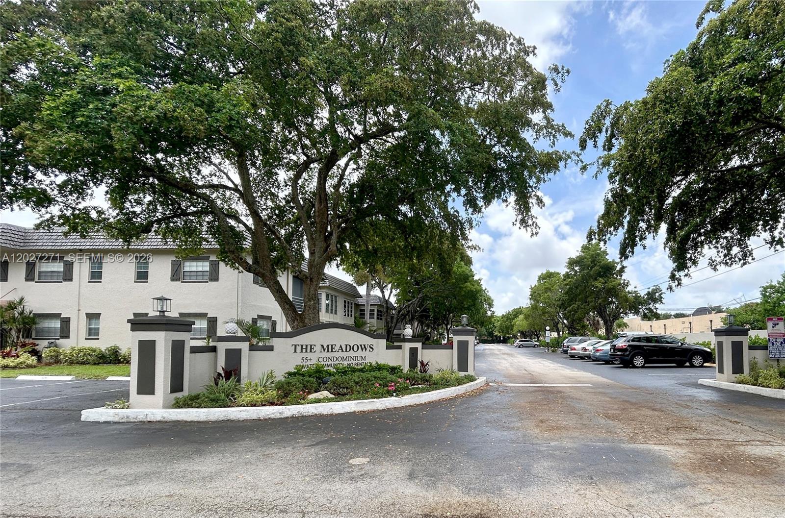 The entrance to The Meadows 55+ condominium community features a sign, landscaping, and parking area — 5621 SW 2nd Ct # 101, Margate FL 33068, MARGATE, FL