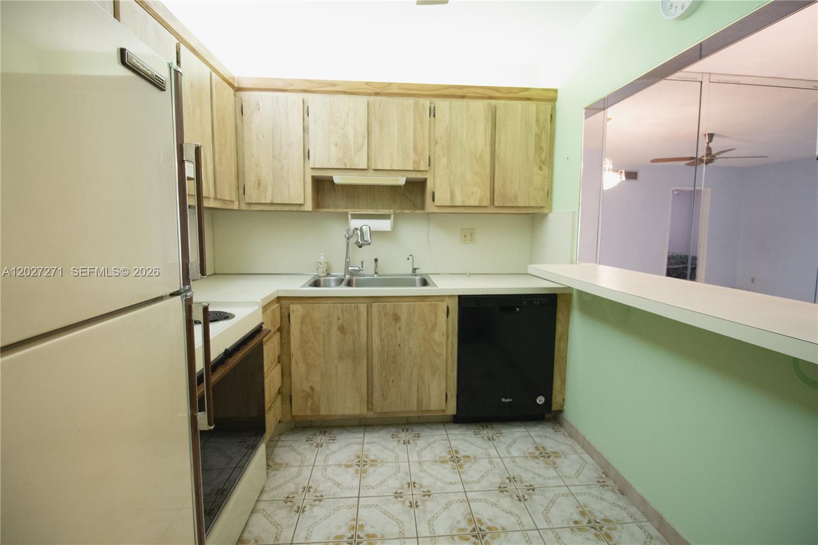 A kitchen features light wood cabinets, a black dishwasher, and a pass-through window — 5621 SW 2nd Ct # 101, Margate FL 33068, MARGATE, FL