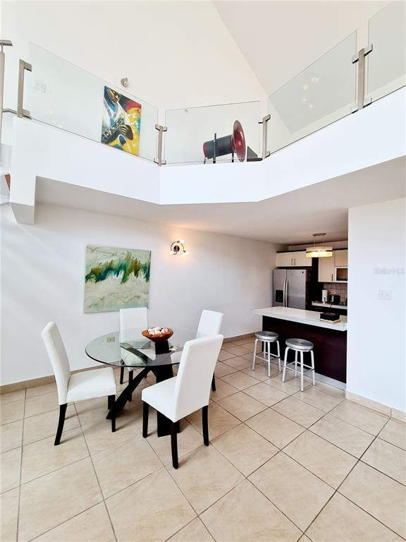 A dining area with a glass table and white chairs sits beneath a glass-railed loft — 500 CALLE ANDALUCÍA UNIT 508-4, AGUADILLA, PR