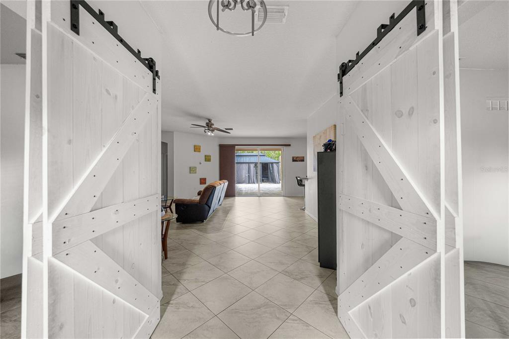 A view through white barn doors into a living area with tiled floors and sliding doors — 8778 SW 127TH AVENUE, DUNNELLON, FL