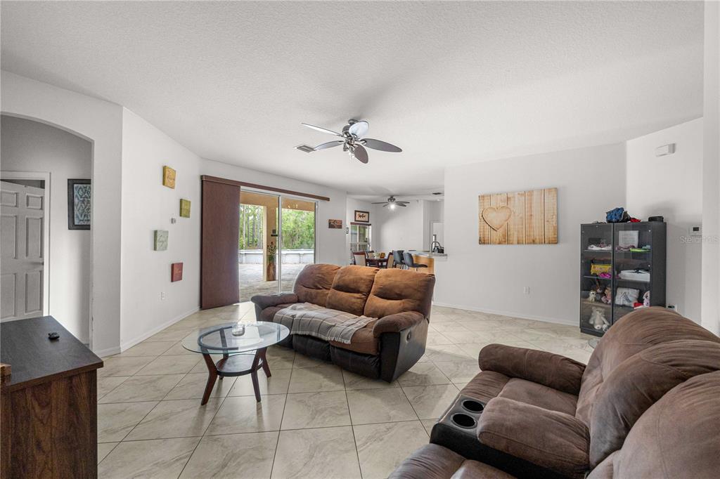 A living room with tile flooring, two brown sofas, and a sliding glass door — 8778 SW 127TH AVENUE, DUNNELLON, FL