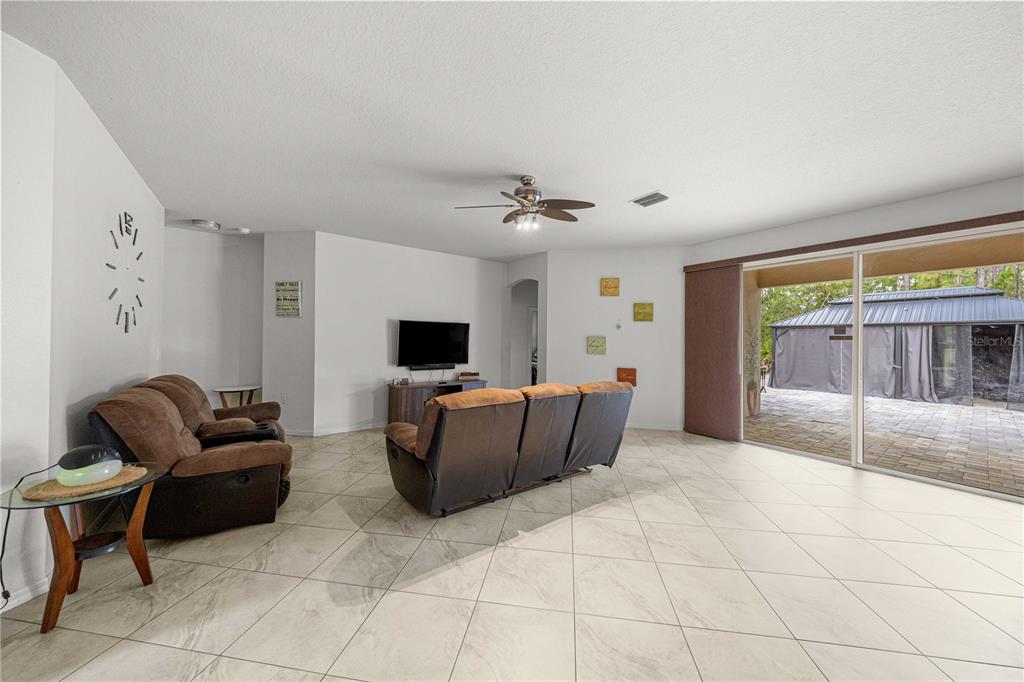 A living room features light tile flooring, brown reclining furniture, and a large sliding glass door — 8778 SW 127TH AVENUE, DUNNELLON, FL