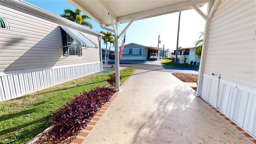 A concrete driveway sits under a carport between two light-colored mobile homes — 10100 BURNT STORE ROAD UNIT 123, PUNTA GORDA, FL
