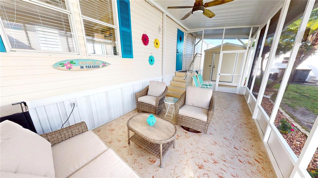 A screened-in porch features wicker furniture, a ceiling fan, and a surfboard wall decoration — 10100 BURNT STORE ROAD UNIT 123, PUNTA GORDA, FL