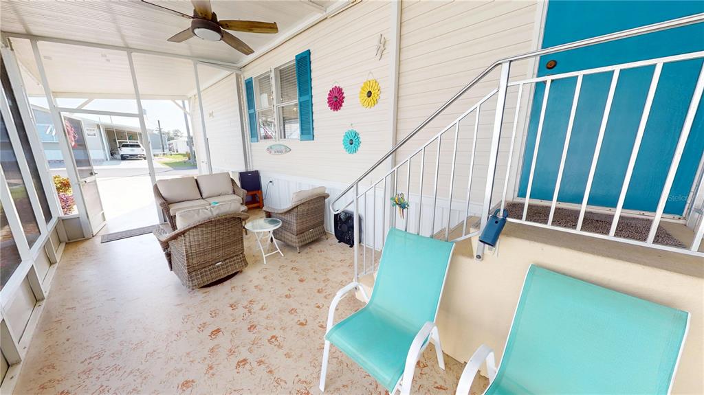 A screened-in porch features wicker furniture, teal chairs, and stairs leading to a blue door — 10100 BURNT STORE ROAD UNIT 123, PUNTA GORDA, FL