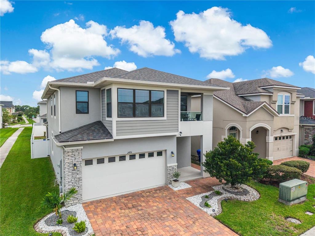 A two-story house with a gray stucco exterior, stone accents, and a paved driveway — 2495 RAPOLLO DRIVE, KISSIMMEE, FL