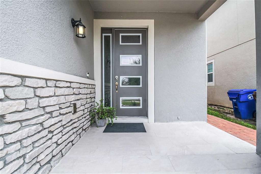 A gray front door with four rectangular windows sits on a covered porch with stone siding — 2495 RAPOLLO DRIVE, KISSIMMEE, FL