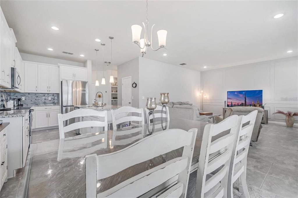 A dining area with white chairs overlooks an open-concept kitchen and living room — 2495 RAPOLLO DRIVE, KISSIMMEE, FL