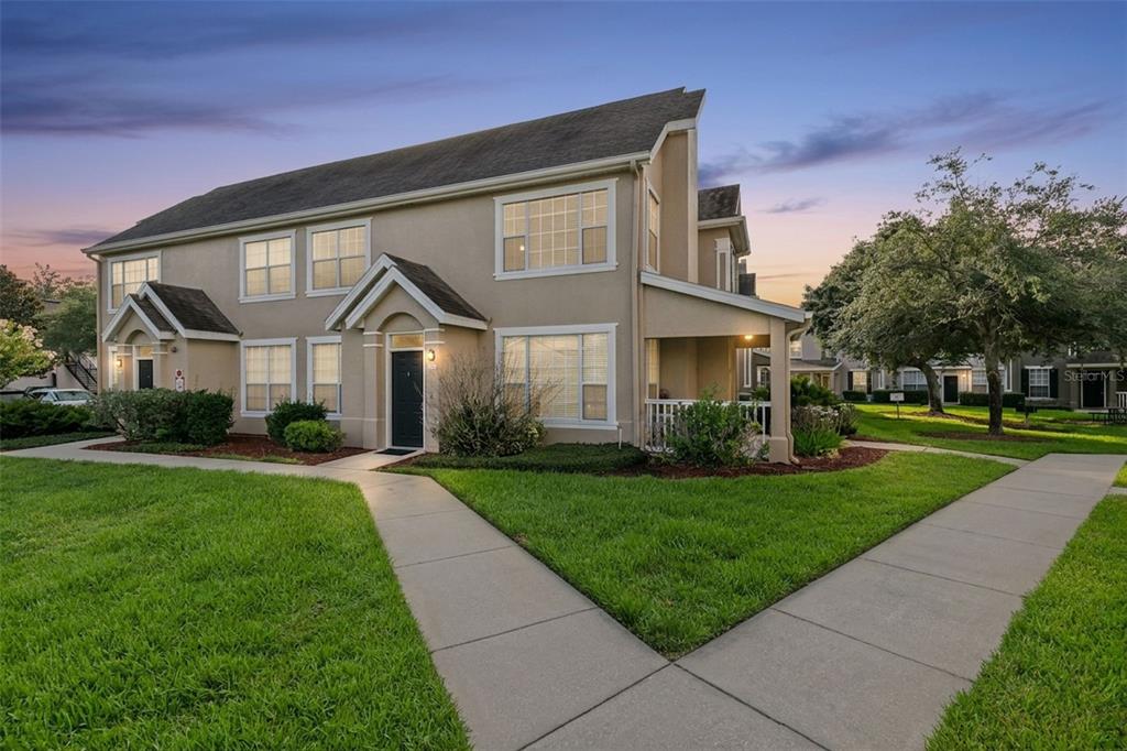 A two-story tan townhouse with a covered porch and a concrete walkway in front — 9125 LEE VISTA BOULEVARD UNIT 704, ORLANDO, FL