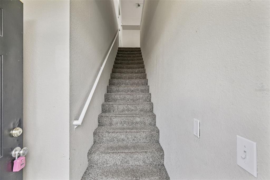 A straight carpeted staircase leads upward between two plain, light-colored walls — 9125 LEE VISTA BOULEVARD UNIT 704, ORLANDO, FL