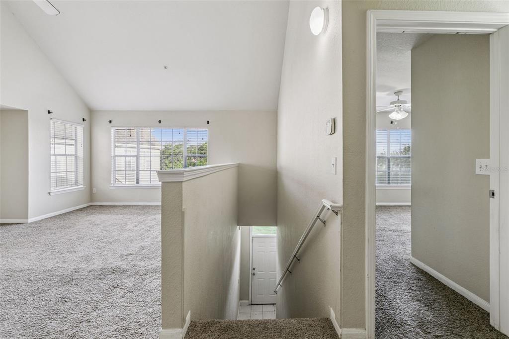 An interior view shows a carpeted landing area with stairs leading down to a door — 9125 LEE VISTA BOULEVARD UNIT 704, ORLANDO, FL