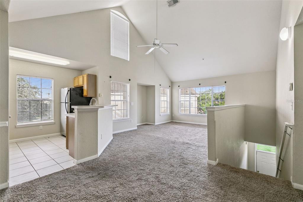 An open-concept living area with vaulted ceilings, carpeted floors, and an adjacent tiled kitchen — 9125 LEE VISTA BOULEVARD UNIT 704, ORLANDO, FL