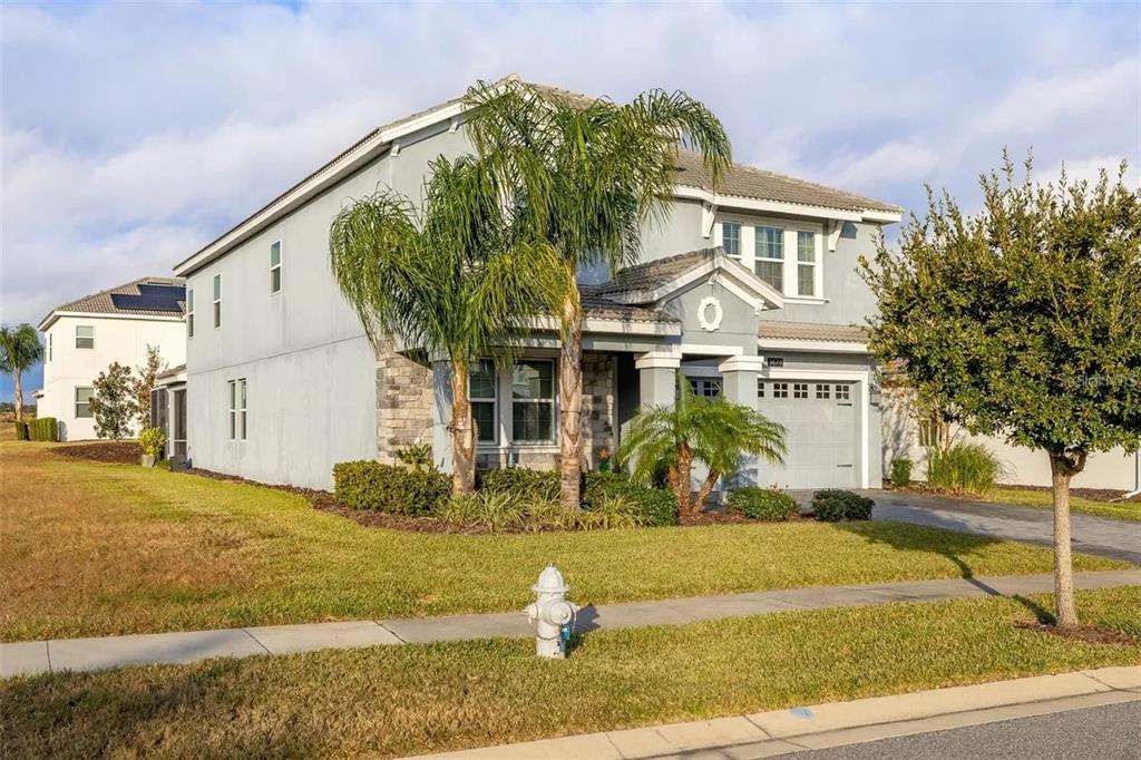 A two-story suburban house with a gray stucco exterior, stone accents, and a palm tree — 1474 OLYMPIC CLUB BOULEVARD, CHAMPIONS GATE, FL