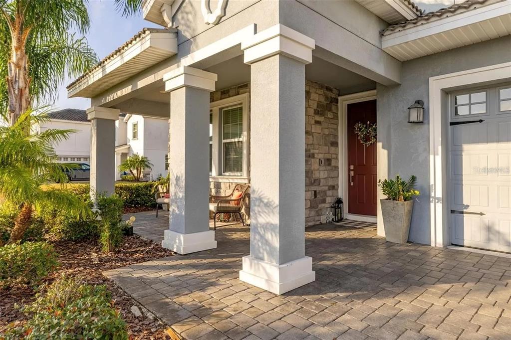 A gray house exterior features a stone-accented entryway, a red front door, and paved porch — 1474 OLYMPIC CLUB BOULEVARD, CHAMPIONS GATE, FL