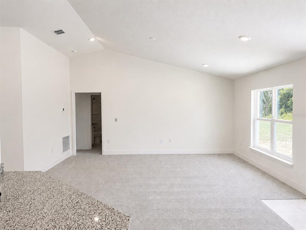 An empty room with vaulted ceilings, gray carpet, and a doorway leading to a bathroom — 1680 ANN ROSE WAY WAY, LEESBURG, FL