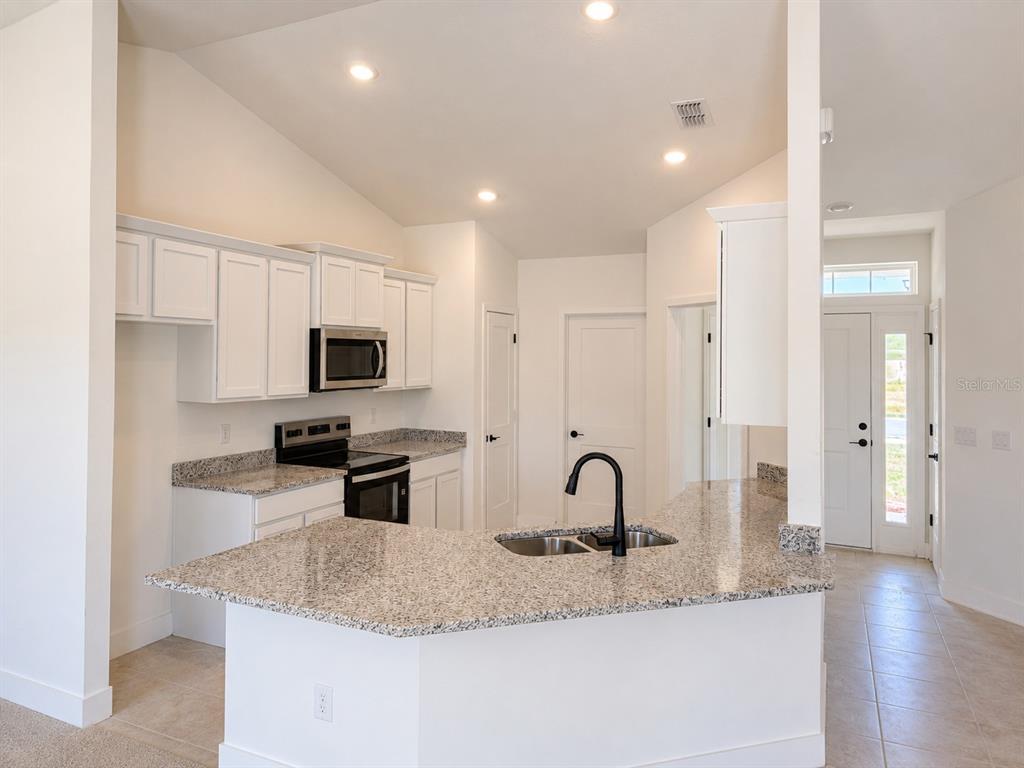A kitchen features white cabinets, granite countertops, a stainless steel stove, and a black faucet — 1680 ANN ROSE WAY WAY, LEESBURG, FL