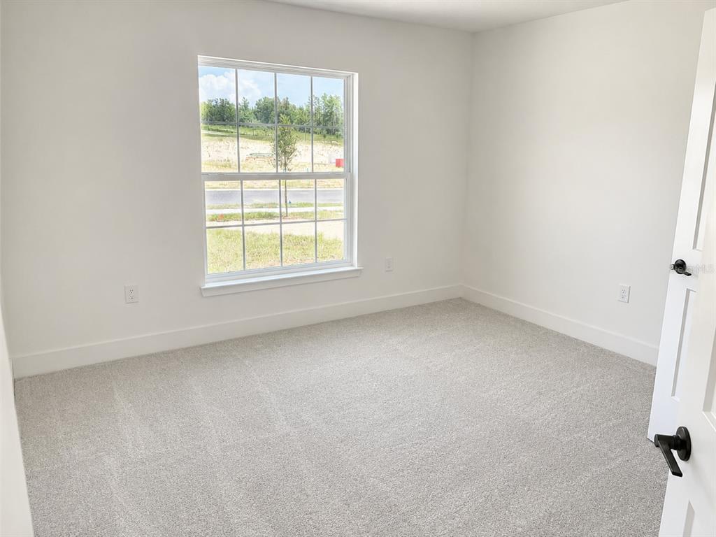 An empty bedroom features white walls, light gray carpeting, and a window with exterior views — 1680 ANN ROSE WAY WAY, LEESBURG, FL