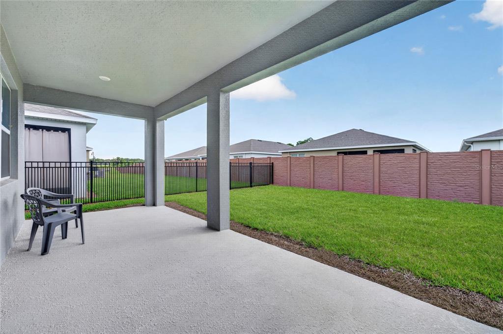 A covered concrete patio overlooks a fenced backyard with a green lawn — 4975 NW 39TH LOOP, OCALA, FL