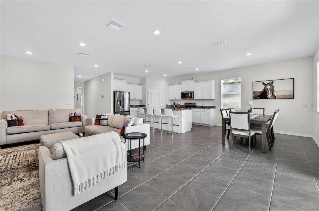 An open-concept living room and kitchen featuring white cabinetry, tile flooring, and neutral furniture — 4975 NW 39TH LOOP, OCALA, FL